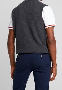 Grå stickad väst med rund halsringning, bärs över en vit polo med röda och marinblå ränder, i kombination med marinblå byxor.