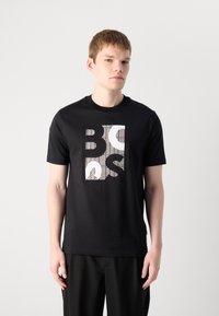 Svart bomull T-skjorte med et geometrisk grafisk design i hvite og oransje nyanser. Korte ermer og rund hals. Glatt tekstur.