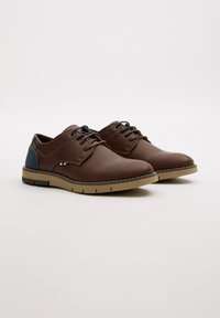 Zapatos de cuero marrón con una textura suave, puntera redondeada y suela de goma beige. Presentan detalles en azul marino y un diseño tradicional con cordones.