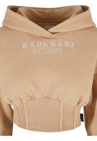 Felpa con cappuccio accorciata in beige chiaro, realizzata in tessuto morbido. Presenta un orlo a costine e il logo ricamato bianco "KARL KANI EST. 1989" sul petto.