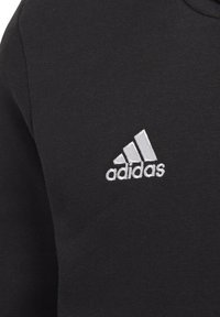 Maglione nero in tessuto con un piccolo logo Adidas ricamato in bianco con tre strisce, posizionato nella zona sinistra del petto.
