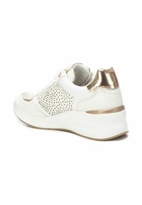 Zapatilla blanca con detalles metálicos dorados, paneles laterales perforados y una suela blanca gruesa. Superficie texturizada en la puntera y el talón.