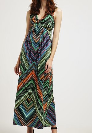 Ærmeløs maxikjole med levende geometrisk mønster i grøn, blå, orange og lilla, båret af stående kvinde med løst hår.