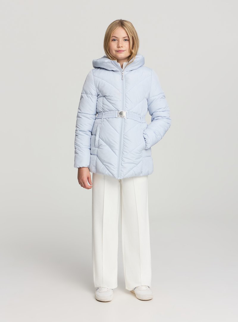 Giacca imbottita azzurro chiaro con cappuccio, cintura in vita e chiusura con zip; presenta trapuntature diagonali e due tasche laterali. Abbinata a pantaloni bianchi a gamba larga.