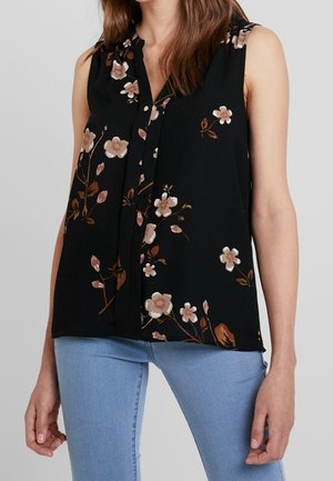 Ärmellose schwarze Bluse mit rosa-braunem Blumenmuster, durchgehend mit Knöpfen, getragen zu hellblauen Jeans.