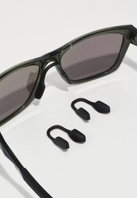 Gafas de sol con un marco de plástico verde oscuro y lentes de color gris; incluye dos piezas de goma negra en las orejas para un ajuste seguro.