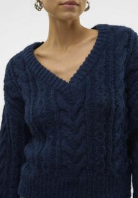 Navy blue knitted sweater with a V-neck, featuring a textured cable pattern and ribbed cuffs. The fabric appears soft and thick.