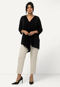 Blusa nera con scollatura a V e maniche a tre quarti, abbinata a pantaloni beige slim-fit e scarpe nere con tacco alto. Tessuto morbido, vestibilità rilassata.