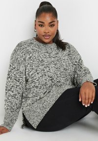 Grå och svart mönstrad oversized sweater med rund halsringning och sidofickor, ihop med svarta byxor. Texturen verkar vara stickad.