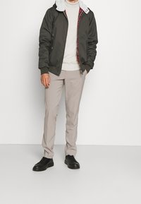 Grön bomberjacka med en fuskpälskrage, buren över en ljus tröja, tillsammans med ljusbeige byxor och svarta skor.