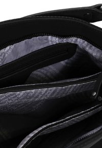 Intérieur d'un sac à main noir montrant plusieurs compartiments zippés et une doublure en tissu gris avec un motif de texte blanc.
