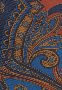 Tyger med ett paisleymönster i blått, orange och brunt. Tyget har en strukturerad väv och intrikata blomster- och svängande mönster.
