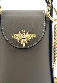Schwarze Lederhandtasche mit einem goldenen Bienenemblem auf dem Deckel, mit einer strukturierten Oberfläche und einem Kettenriemen zum Tragen.