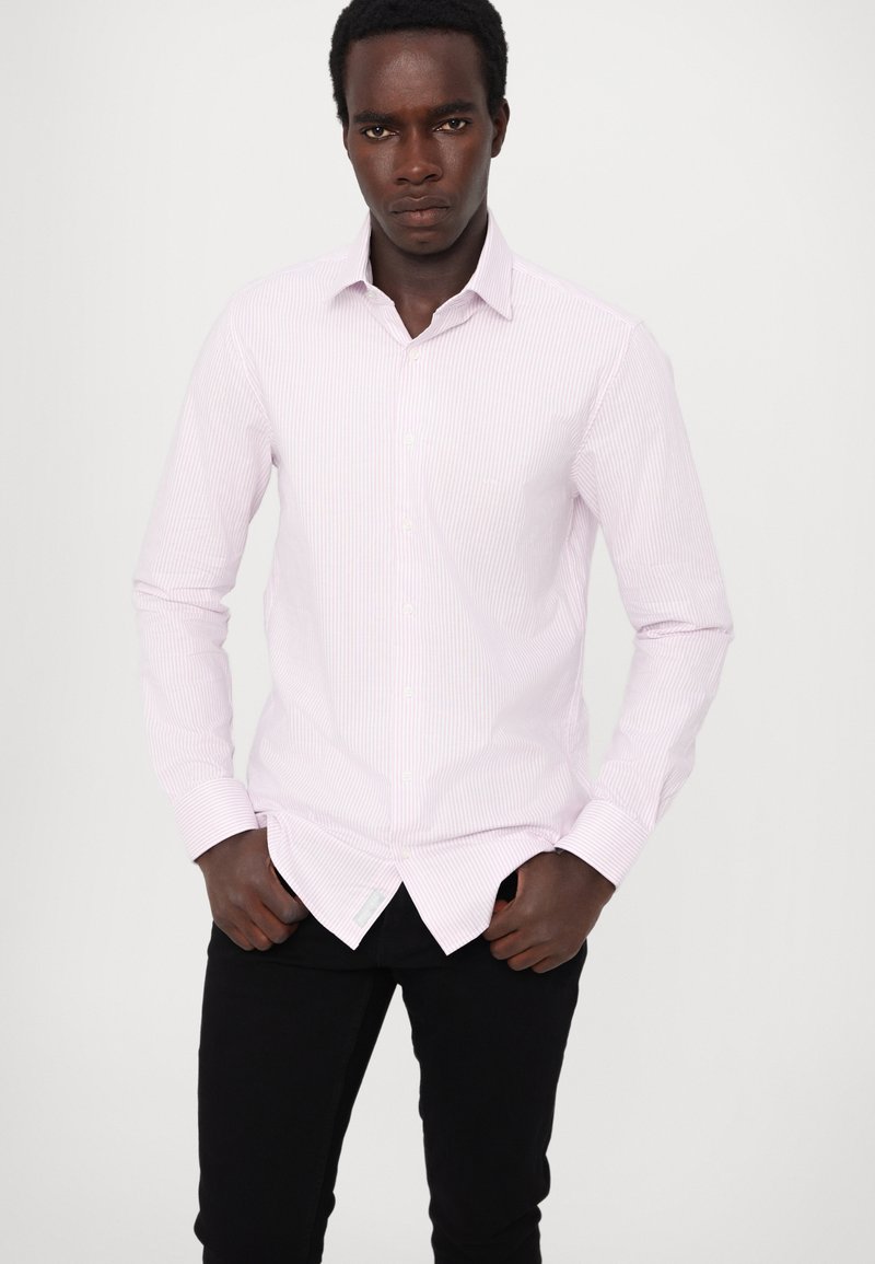 Hellrosa gestreifte Hemdbluse mit langen Ärmeln, Kragen und weißen Knöpfen. Kombiniert mit schwarzen Hosen, schmaler Passform und knitterfreier Stofftextur.