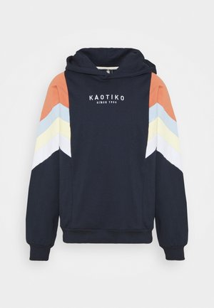 Navy hoodie with multicolor chevron stripes on sleeves, featuring "KAOTIKO SINCE 1999" text on the chest and a front pocket.