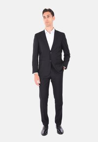 Completo nero su misura con chiusura a due bottoni, rever a lardar e abbinato a una camicia bianca e scarpe eleganti nere lucide. Taglio slim fit.