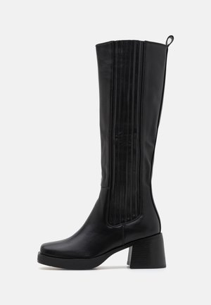 Bottines noires montantes en cuir lisse, présentant des accents en relief verticaux, un talon épais et un design à bout arrondi.
