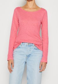 Langärmliges, pinkes Oberteil mit einem u-ausschnitt, weichem Textur und subtilen Wellenmuster, kombiniert mit hellblauen Jeans mit hoher Taille.