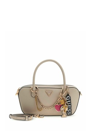 Sac à main beige avec accents en chaîne dorée, présentant un logo triangulaire, une sangle détachable et des breloques décoratives. Texture lisse et forme structurée.