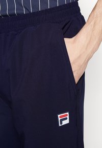 Navy sportshorts met een elastische tailleband en zijzakken; heeft een opvallende Fila-logo patch in rood, wit en blauw.