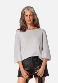 Lichtgrijze, lange mouwen top met een brede halslijn en textuurstof, gecombineerd met hoge zwarte leren shorts.
