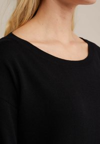 Mustvalge kootud sviiter laia ümmarguse kaelusega ja tekstureeritud kangaga. Disainis on langenud õlad, mis loovad mugava istuvuse.