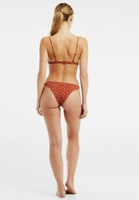 Bruin bikini met stippen, met dunne bandjes, voorzien van een haaksluiting op de rug en een laag uitgesneden onderkant, gemaakt van gladde stof.