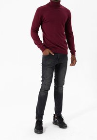Suéter burdeos de cuello alto con dobladillo acanalado, combinado con jeans negros desgastados que presentan detalles rasgados, y zapatillas deportivas negras.