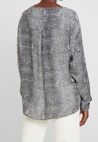 Koszula z długim rękawem w czarno-białym kolorze z teksturowanym, abstrakcyjnym wzorem. Charakteryzuje się luźnym krojem i subtelną plisą z tyłu.