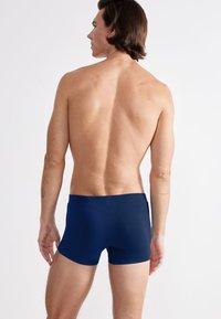 Dunkelblaue Boxer-Shorts aus glattem Stoff, mit tailliertem Design, elastischem Bund und minimaler Nahtdetails auf der Rückseite.