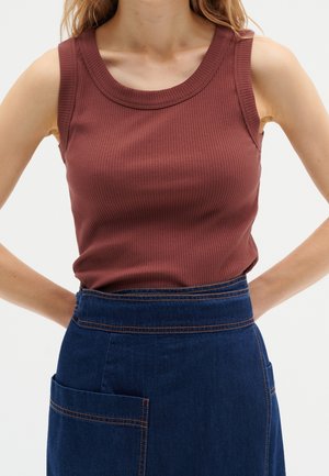 Top sin mangas de color óxido con diseño acanalado y escote redondo, combinado con una falda de mezclilla azul oscura que presenta costuras visibles y un bolsillo frontal.