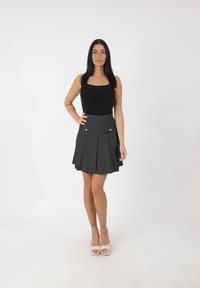 Top nero aderente abbinato a una gonna grigia plissettata con due tasche frontali e dettagli con bottoni argento; la modella indossa sandali con cinturini.