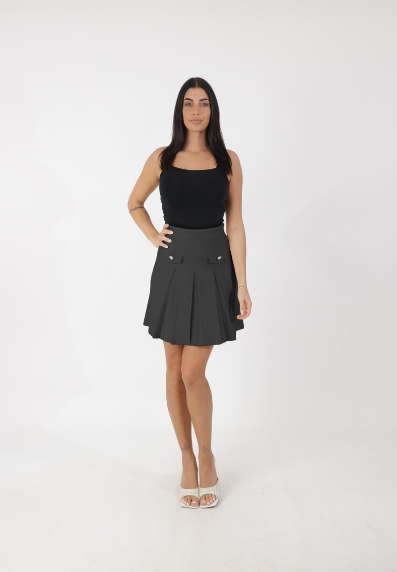 Top nero aderente abbinato a una gonna grigia plissettata con due tasche frontali e dettagli con bottoni argento; la modella indossa sandali con cinturini.