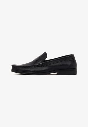 Zapato mocasín de cuero negro para hombre con tacón bajo y costuras tipo moc toe, mostrado en perfil lateral sobre fondo blanco.