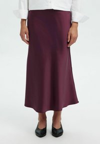 Gonna midi in satin bordeaux con una texture liscia e una silhouette fluida, abbinata a ballerine nere. L'orlo è leggermente curvo nella parte inferiore.
