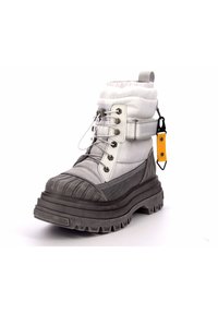 Botín de tobillo blanco y gris con parte superior acolchada, cap toe de goma, panel lateral texturizado, cordones y una etiqueta amarilla. Suela negra gruesa y estriada.