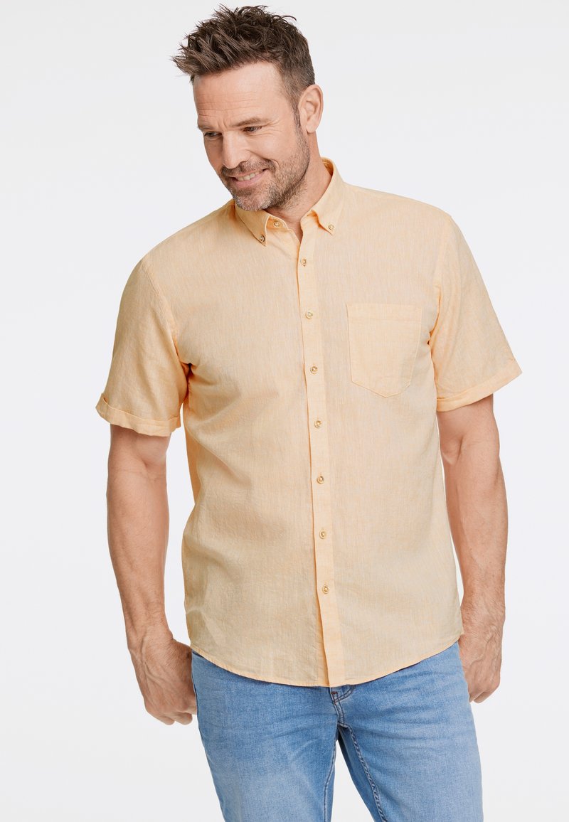 Camisa de manga corta con botones en tela de color naranja claro con una textura sutil, que cuenta con un bolsillo en el pecho y un dobladillo curvo.
