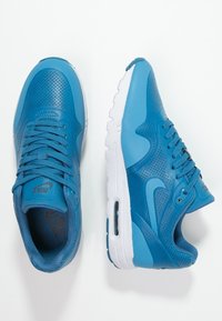 Un paio di sneakers Nike blu con suole bianche, dettagli perforati e lacci, viste dall'alto e di lato su uno sfondo bianco.