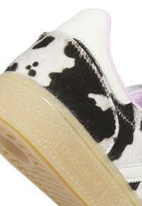 Teri pilkupüüdev musta-valge lehmakarjamaustriga tossu konts, valgete nahkaktsentide ja läbipaistvast kummist tallaga, millel on pressitud Adidas logo.