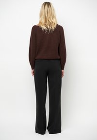 Bruine gebreide trui met verlaagde schouders, gecombineerd met zwarte wijde broek met zijzakken en een zachte textuur.