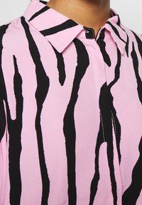 Chemise rose avec des rayures zébrées noires, col pointu, fermeture éclair à l'avant et texture de tissu lisse.