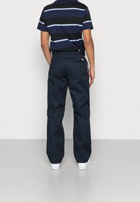 Pantalons larges bleu marine au toucher lisse, associés à une chemise à manches courtes rayée noire et bleu marine. Des baskets blanches complètent le look.