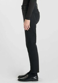 Jeans de mezclilla negra con un diseño ajustado, que presentan una textura suave, bolsillos estándar y una cintura baja, combinados con zapatos negros.