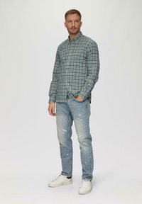 Geklede blouse met ruitmotief in groene en blauwe tinten, licht beschadigde jeans en witte sneakers. Casual pasvorm met lange mouwen en een reguliere kraag.