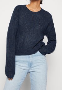 Pull tricoté bleu marine avec un motif texturé, col rond et manches longues, associé à un jean taille haute bleu clair.