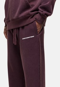 Bordeaux joggingsbroek met voorzakken en een elastische tailleband met trekkoord. Met witte "GOODFORNOTHING" tekst op de linker bovenbeen. Zachte stof.