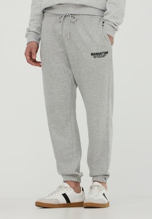 Pantaloni sportivi grigi con vita elastica, tasche laterali e polsini a coste. Presenta il testo nero "MANHATTAN" sulla coscia sinistra.