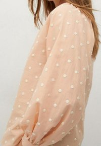 Perzikkleurige blouse met pofmouwen, voorzien van witte geborduurde stippen. Zachte, lichte stof met een gestructureerde uitstraling.