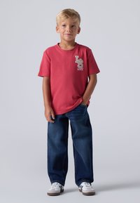 Camiseta de algodón roja con el logo "LS Levi's", combinada con jeans de mezclilla azules y zapatillas blancas con rayas negras. Diseño simple, ajuste relajado.