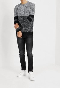 Gehaakt sweater in grijs en zwart, ronde hals, textuurpatroon, geribbelde manchetten, gecombineerd met donkere jeans en witte sneakers.